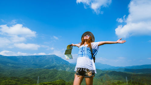 Woman with arms outstretched standing against blue sky