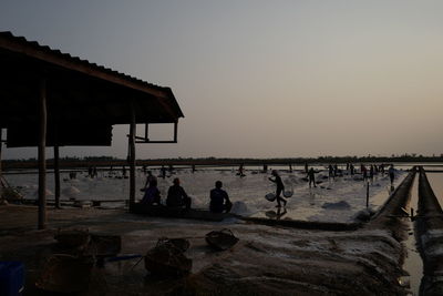 People at beach against clear sky during sunset