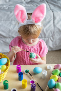 Little girl in easter bunny ears painting colored eggs. easter at home and craft concept.