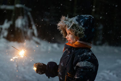 Toddler girl in winter clothes walking outside and holding sparkler in her hand. dark and snowy