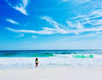 Rear view of woman standing on shore at beach against blue sky