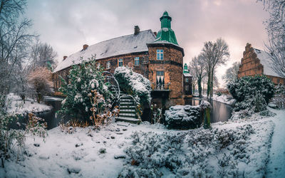 Snow covered houses by building against sky