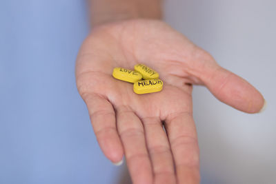 Cropped hand of woman holding yellow flower against blue background