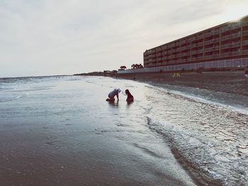 Rear view of people at beach against sky