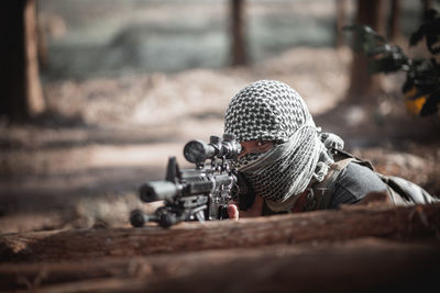 Man wearing headscarf aiming rifle on tree trunk in forest