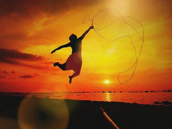 Silhouette man jumping on beach against sky during sunset