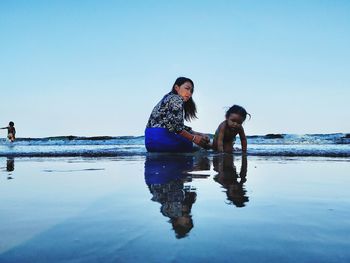 Mother and daughter at beach against clear sky