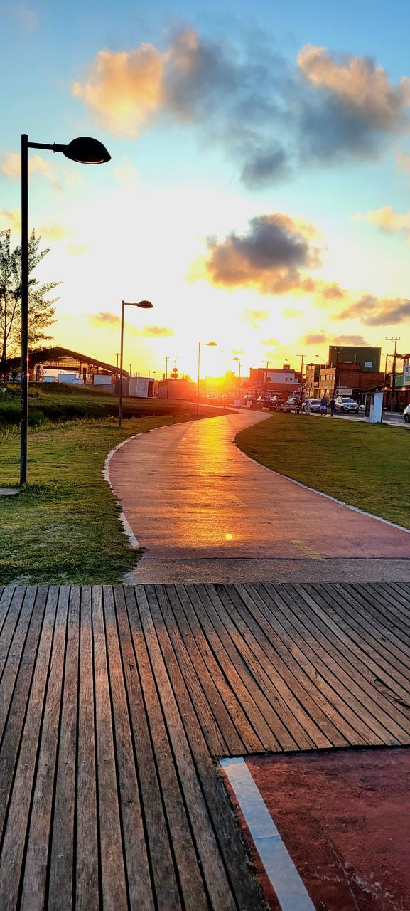 sky, sunset, cloud, walkway, nature, architecture, evening, footpath, street, sunlight, dusk, built structure, no people, boardwalk, outdoors, water, city, street light, wood, building exterior, beauty in nature, horizon, orange color, transportation, sports, sun, pier, plant, tranquility, grass