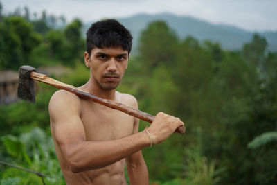 Young handsome shirtless boy holding axe in his shoulders.