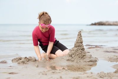 Rear view of woman on rock at beach against sky