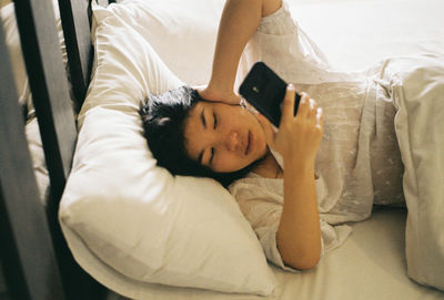 Woman using mobile phone while sleeping on bed at home