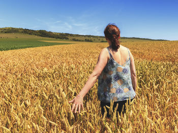 Rear view of woman standing by plants in farm against sky