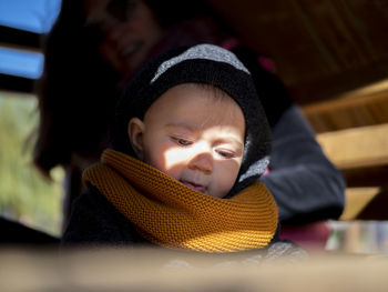 Close-up of cute girl wearing sweater and knit hat sitting with mother at home