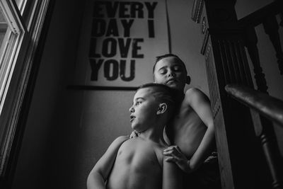 Low angle view of shirtless brothers sitting on steps at home