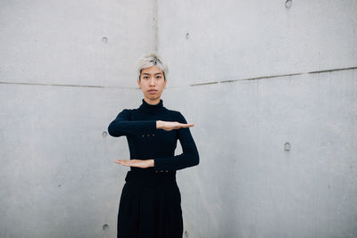 Portrait of woman gesturing while standing against wall