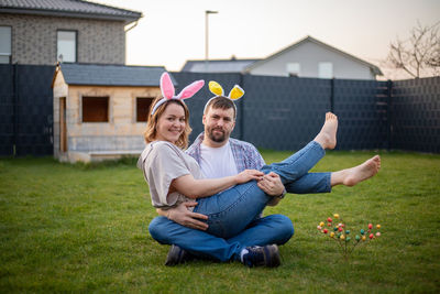 Portrait of couple wearing bunny ears sitting on grass