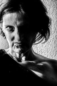 Close-up portrait of angry senior woman against wall