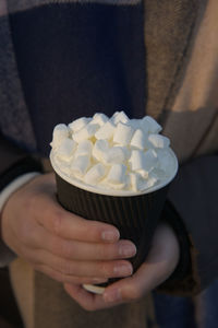 Hot take away beverage with an marshmallows and cream on top, cradled by youthful female hands.