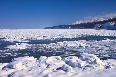 Frozen sea by snowcapped mountain against blue sky