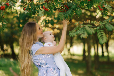 A happy smiling mother holds her little son in her arms and shows him rowan berries