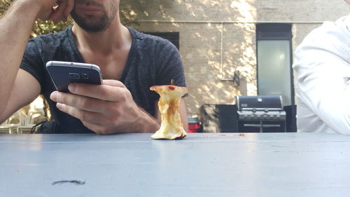 Midsection of man using mobile phone while sitting at table