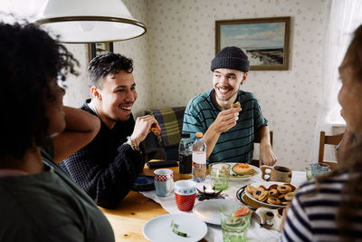 Cheerful friends talking while enjoying food in social gathering at home