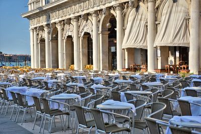 Empty chairs and tables at sidewalk cafe against building