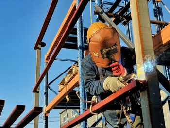 Man working on metal structure against sky