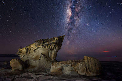 Rock formation at beach against milky way at night