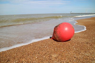 Red ball on sand at beach against sky