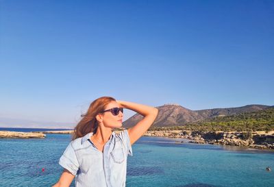 Woman standing by sea against clear blue sky