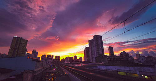 City street by buildings against sky during sunset