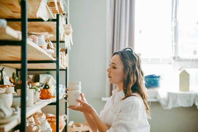 Beautiful middle-aged woman stands at shelf with pottery items