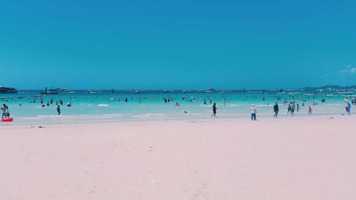 People swimming in sea against clear blue sky