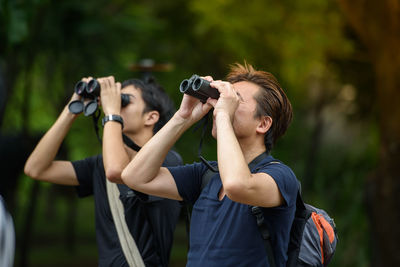 Full length of man holding camera while standing outdoors