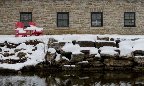 Snow covered chair against brick wall