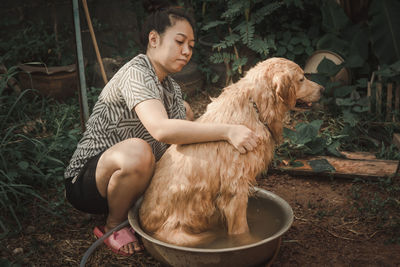 Woman bathing dog against plants