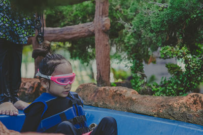 Little girl sitting on the slide in swimming pool. wearing goggles and life jackets.