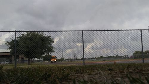 Chainlink fence on field against cloudy sky