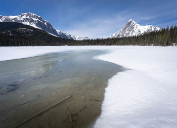 Half frozen alpine lake surrounded by snowy mountains, watridge lake, kananaskis, alberta, canada
