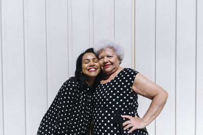 Mother and daughter standing cheek to cheek in front of wall