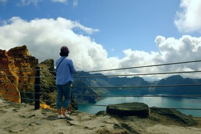 Rear view of man standing by mountain against sky