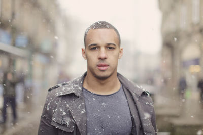Portrait of young man standing on city street during snowfall