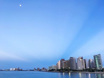 Sea by buildings against blue sky