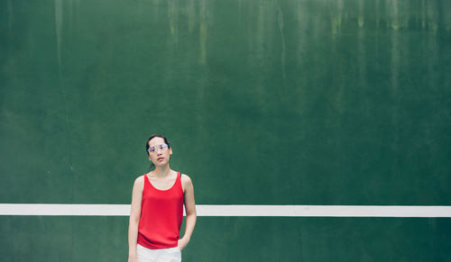 Woman wearing eyeglasses while standing against wall