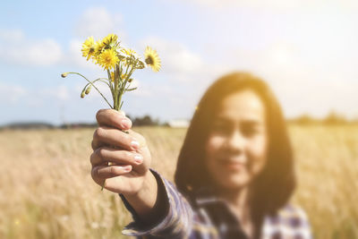 Close-up portrait of woman holding flowers by plants against sky