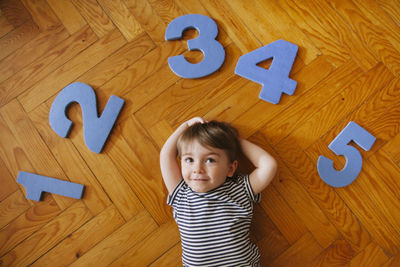 High angle view of cute boy with numbers lying on hardwood floor