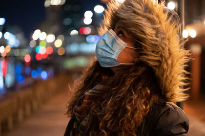 Portrait of woman with illuminated hair at night. wearing a mask at night in the city