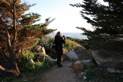 Rear view of woman photographing sea from cliff