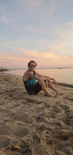 Man wearing sunglasses on beach against sky during sunset